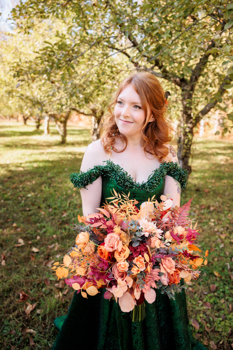Bride holding a faux rust, burgundy and burnt orange bridal bouquet in an emerald green gown.