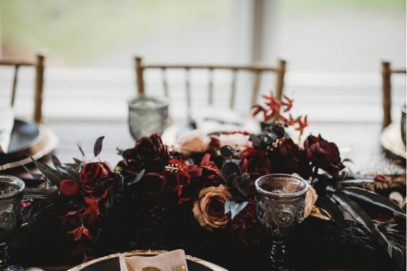 Dark and stylish wedding centerpiece with burgundy blooms and golden touches