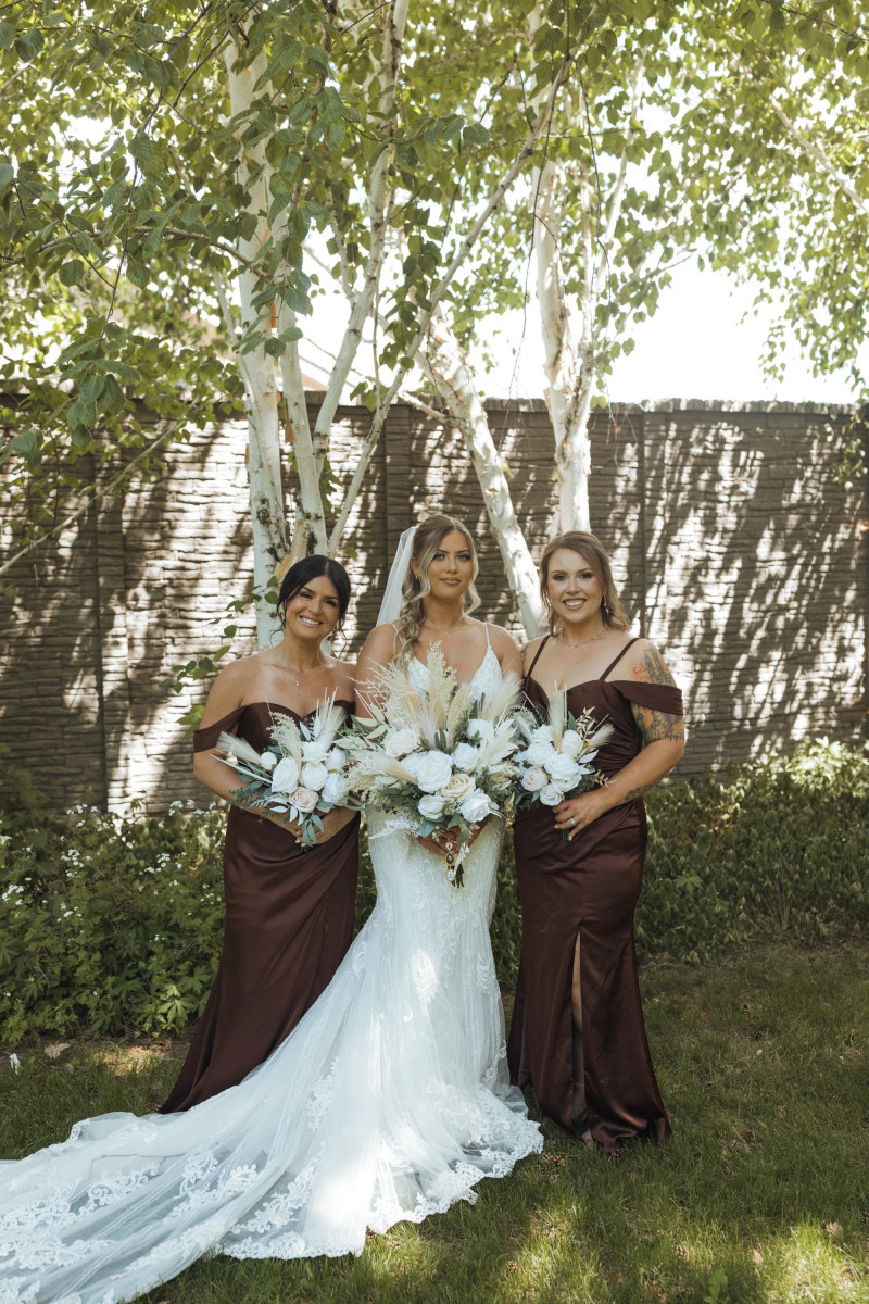Bride with ivory and beige pampas wedding bouquet with bridesmaids in brown dresses outdoors