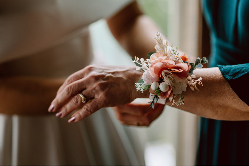 Peach and blush pink wrist corsage with greenery on mother of the bride during wedding preparation
