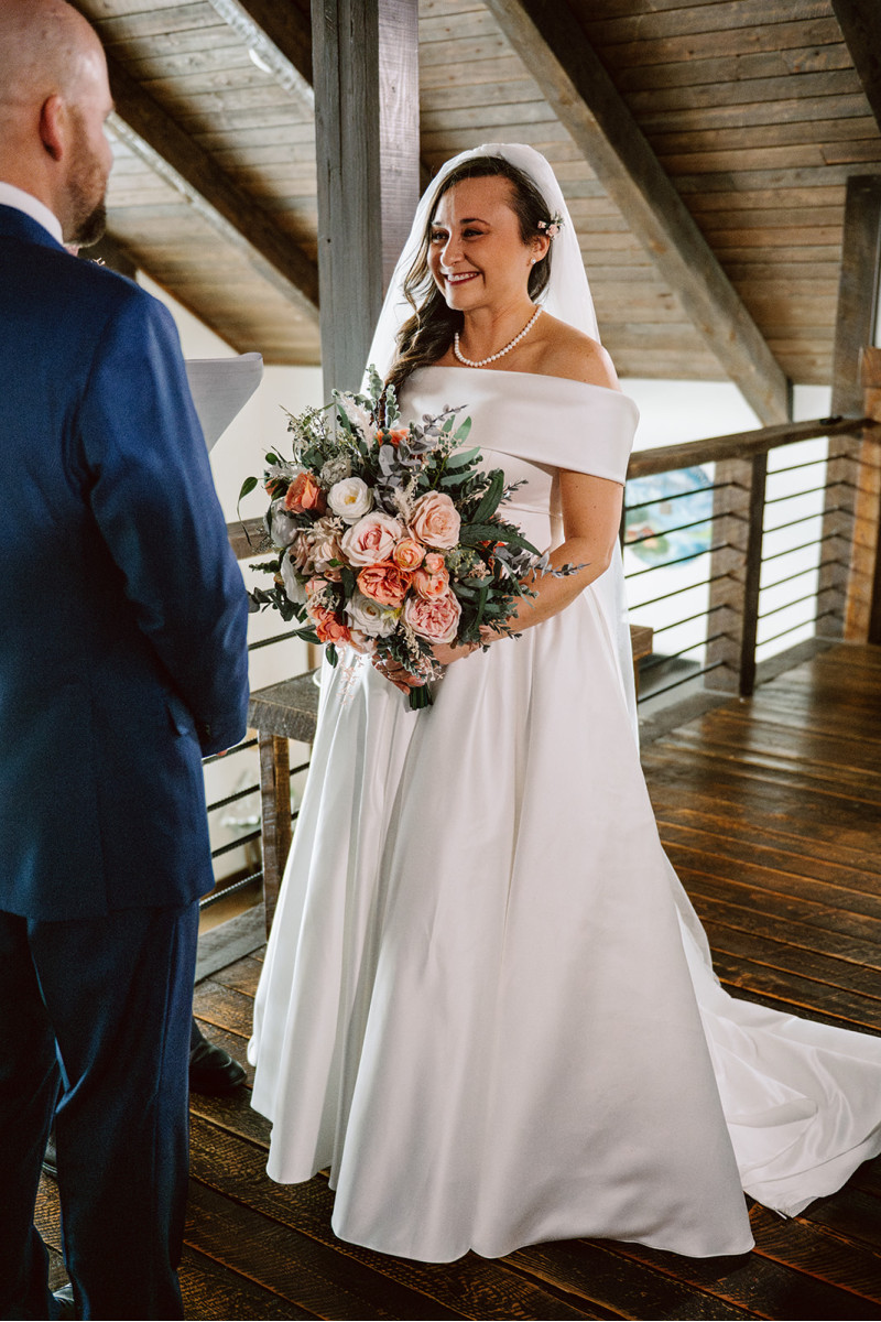 Bride in modern satin wedding gown with peach and blush pink bridal bouquet during ceremony