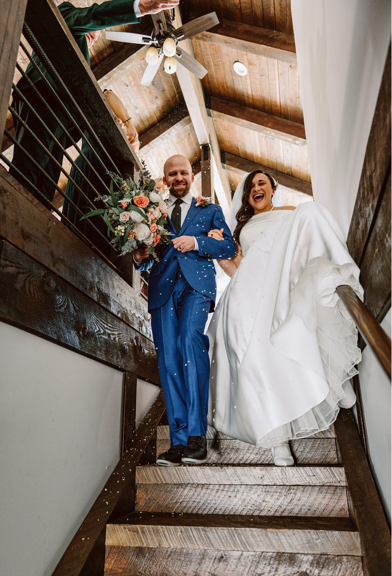 Bride and groom walking down staircase after ceremony with peach and blush pink wedding bouquet