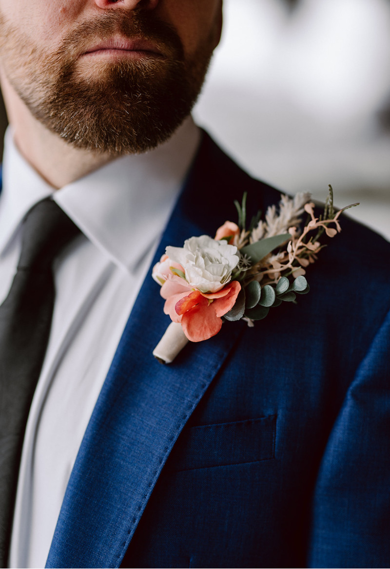 Groom in blue suit with peach and blush pink boutonniere and greenery