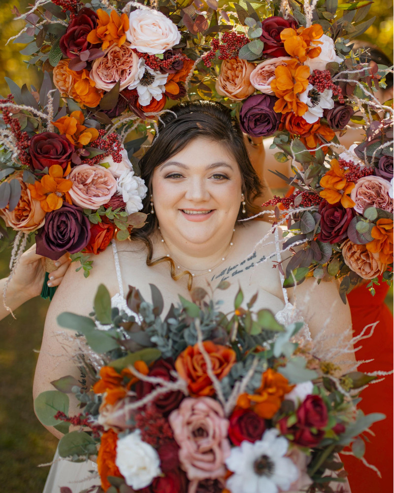 Bridal bouquet surrounded by bridesmaids holding bouquets in burgundy, rust, ivory, and cinnamon colors