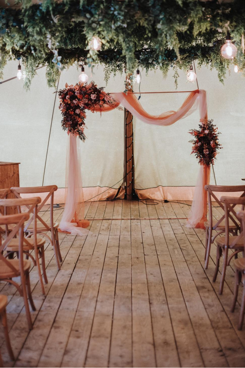 wedding arch with plum, purple, orange, rust and beige floral arrangements and draping