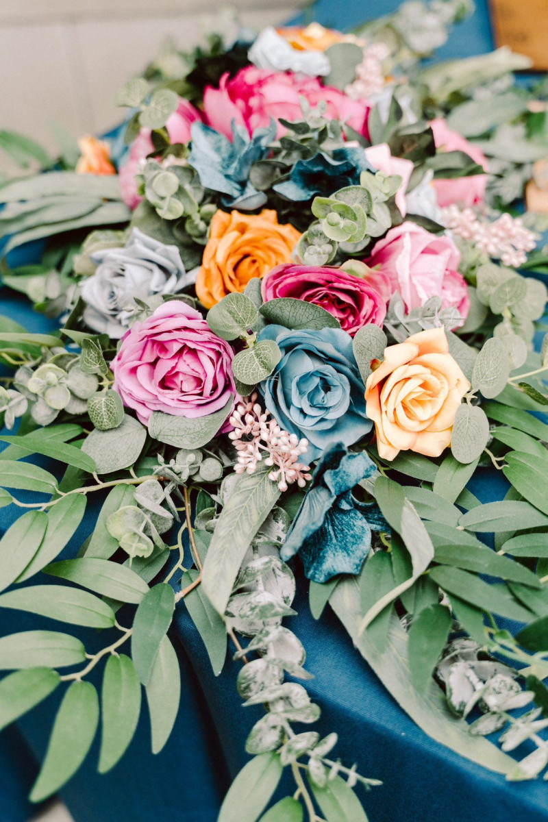 Bold floral arch arrangement featuring teal, magenta, and orange flowers with lush greenery