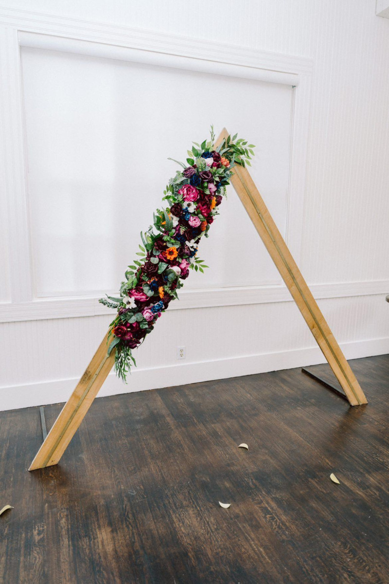 Wedding arch flowers in jewel tones with emerald green, orange, magenta, and teal silk blooms
