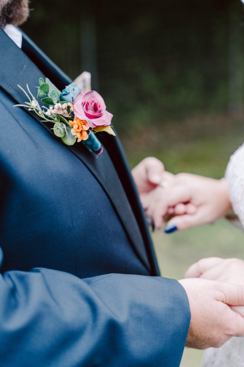 Colorful boutonniere in magenta, teal, and orange with emerald green accents for a vibrant wedding