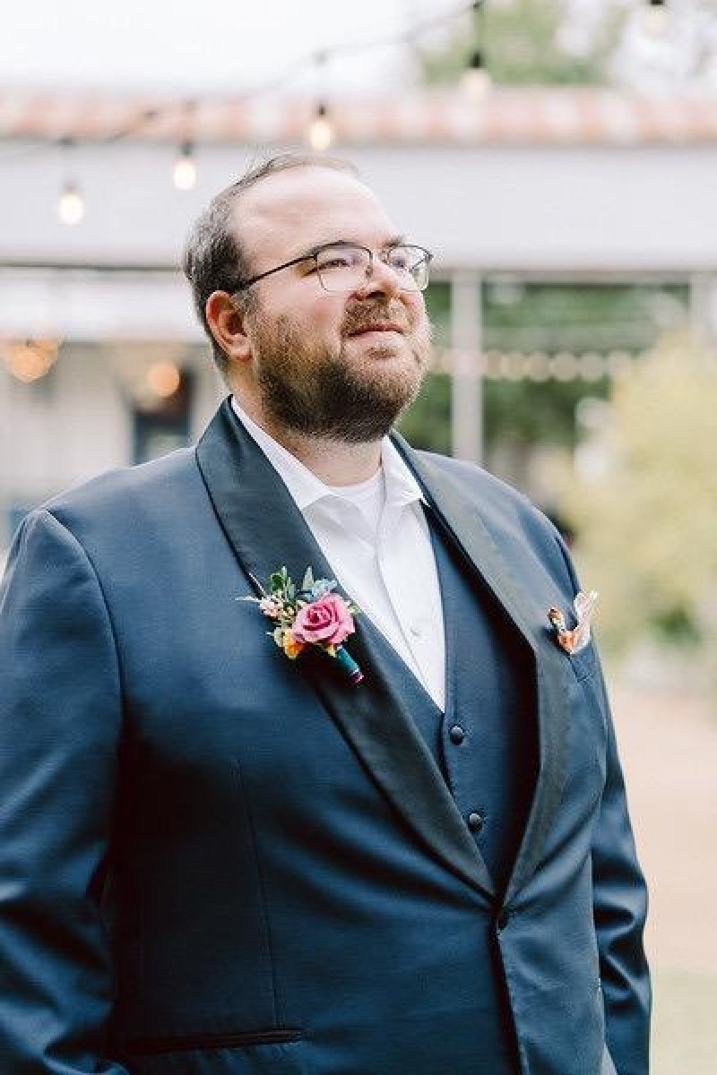 Jewel-tone boutonniere with emerald green, orange, magenta, and teal flowers for the groom