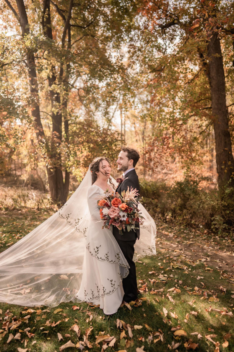 bride and groom in autumn forest with burgundy, rust, ivory and cinnamon wedding bouquet