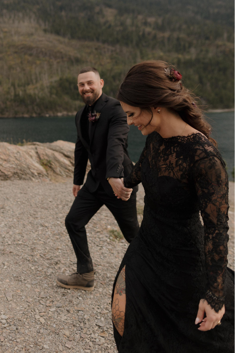 wedding couple walking hand in hand in black outfits, bride wearing hair comb, purple burgundy and gold floral details