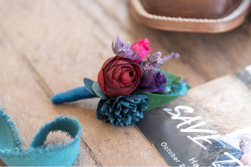 Purple, Teal, Red & Magenta boutonniere, jewel tone wedding details on wooden surface