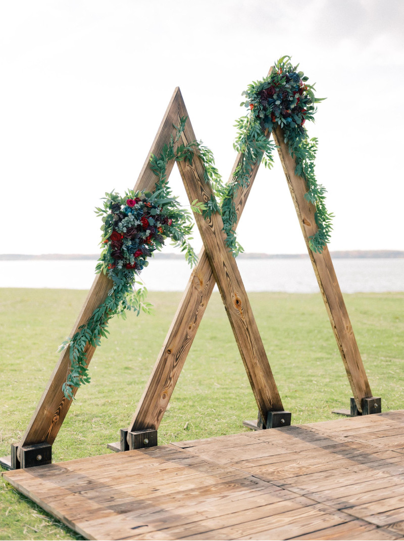 Jewel-tone wedding arch with emerald green, magenta, and teal floral arrangement