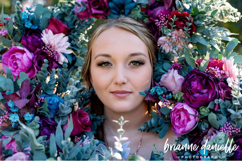 Bride with jewel-tone wedding arch flowers in emerald green, purple, magenta, teal and navy blue
