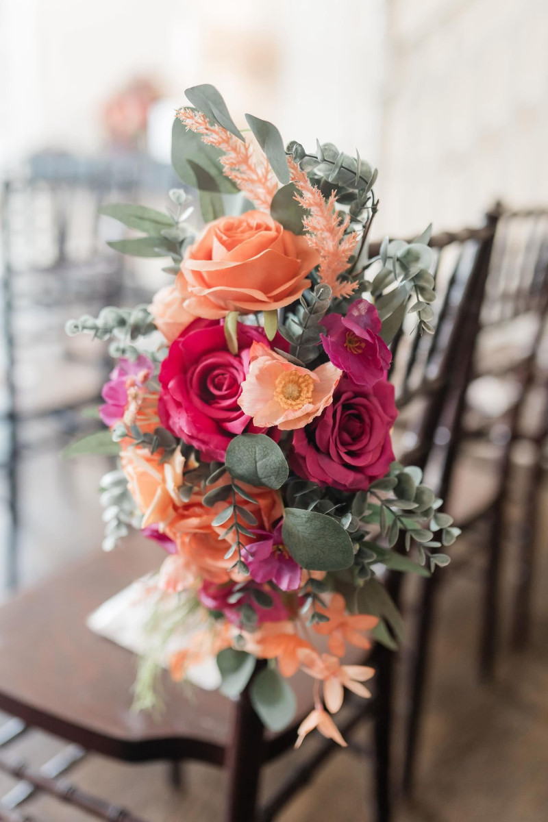 Magenta peach and coral faux floral wedding chair arrangement with roses and greenery