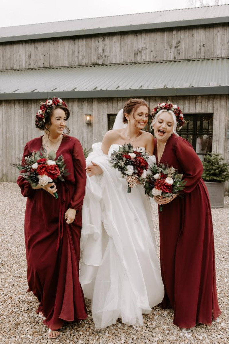 bride with bridesmaids in burgundy dresses wearsng flower crowns and holding black, gold, burgundy and ivory bouquets