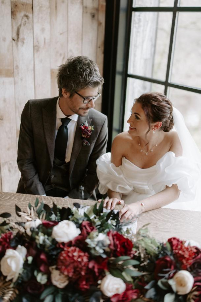 bride and groom seated with black, gold, burgundy and ivory floral centerpiece