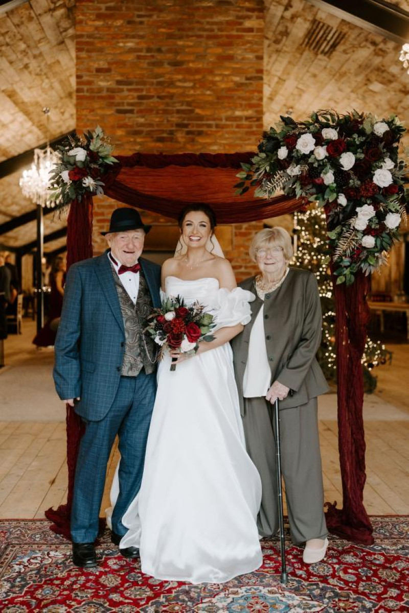bride with family under wedding arch decorated in black, gold, burgundy and ivory flowers